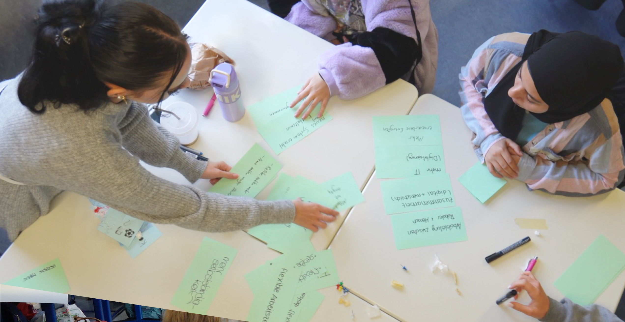 Drei junge Frauen sitzen an einem Tisch und arbeiten gemeinsam mit beschrifteten Moderationskarten.